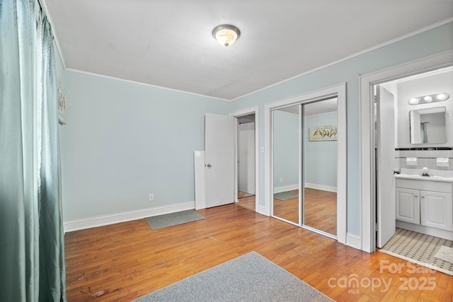 bedroom with connected bathroom, crown molding, baseboards, light wood-style floors, and a sink