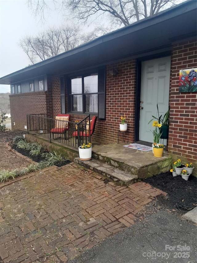 entrance to property with a porch and brick siding