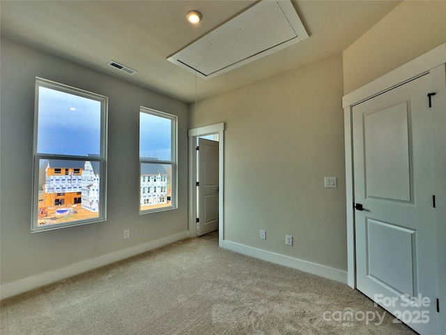 unfurnished room featuring visible vents, carpet flooring, attic access, and baseboards