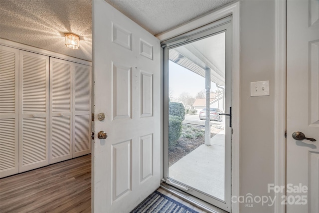 doorway to outside with a textured ceiling and wood finished floors