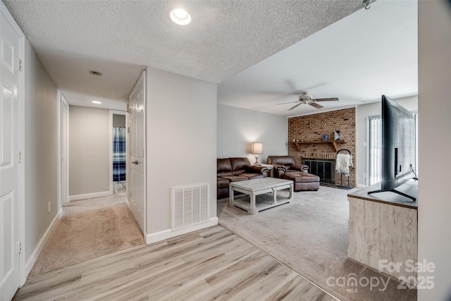 living room with visible vents, ceiling fan, a fireplace, wood finished floors, and a textured ceiling