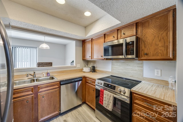 kitchen featuring a sink, stainless steel appliances, light wood finished floors, a raised ceiling, and light countertops