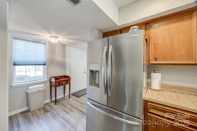 kitchen with brown cabinetry, stainless steel fridge, a textured ceiling, and light wood-style floors