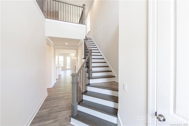 stairs featuring wood finished floors, baseboards, and a towering ceiling