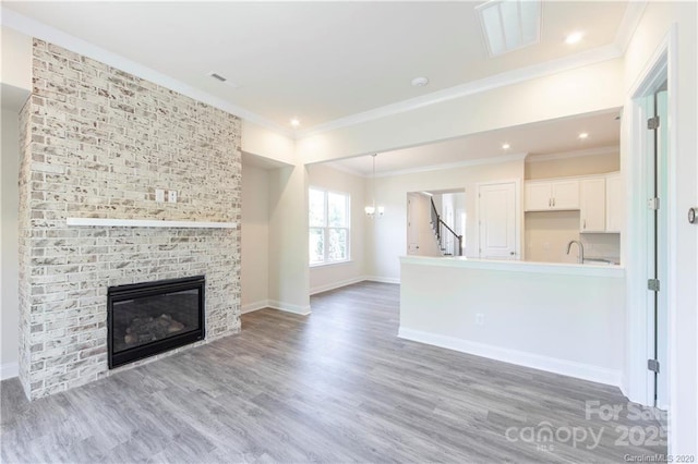 unfurnished living room with an inviting chandelier, crown molding, wood finished floors, and visible vents