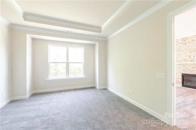 carpeted spare room featuring a tray ceiling, baseboards, and ornamental molding