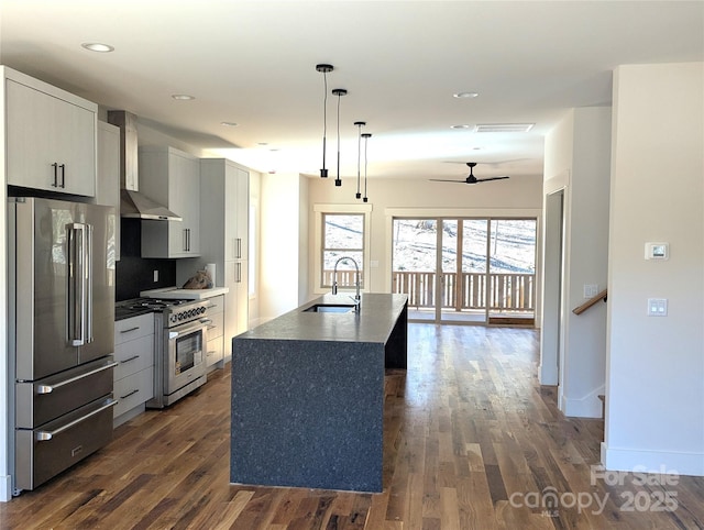 kitchen featuring high quality appliances, a sink, dark wood-style floors, wall chimney range hood, and ceiling fan