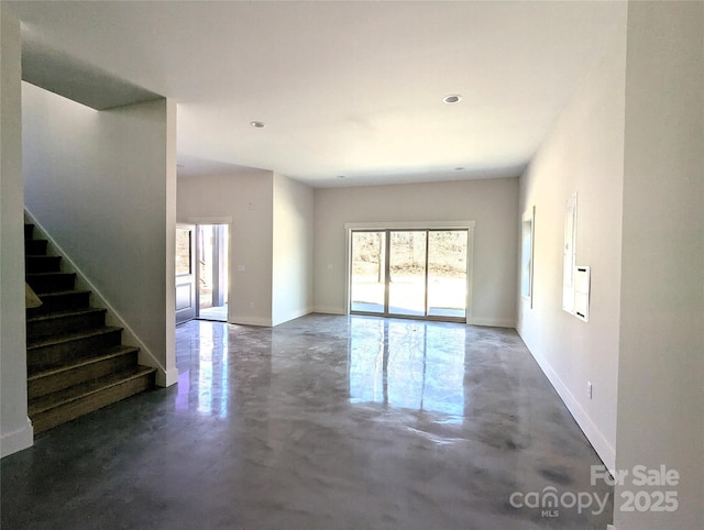 unfurnished living room featuring stairway, concrete flooring, and baseboards