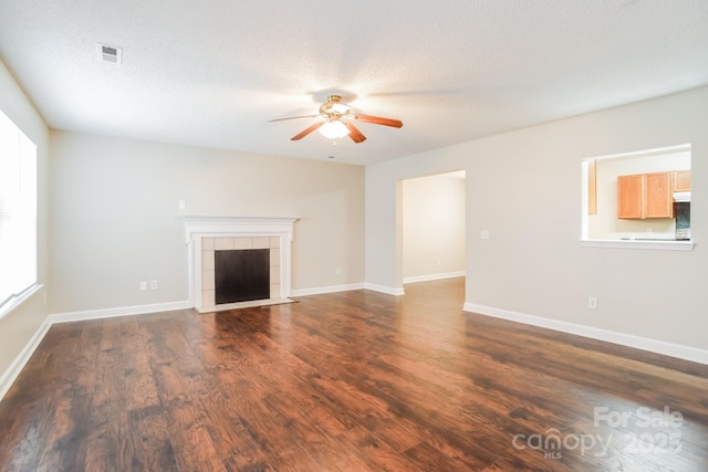 unfurnished living room featuring visible vents, a ceiling fan, baseboards, dark wood-style flooring, and a tile fireplace