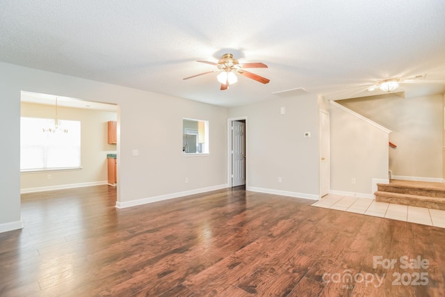 unfurnished living room featuring stairway, a textured ceiling, wood finished floors, and ceiling fan with notable chandelier