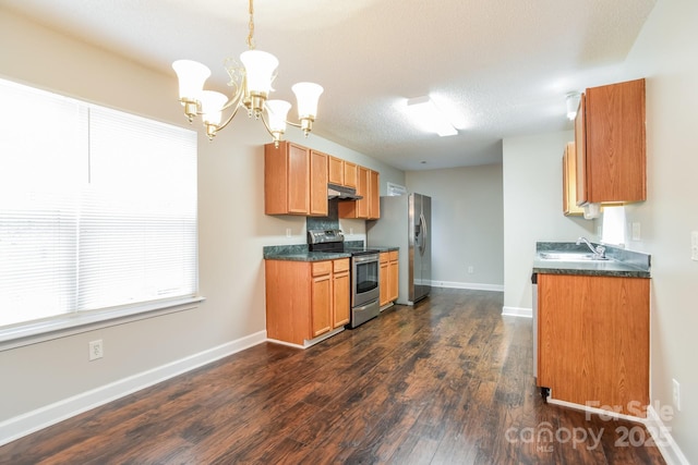 kitchen with under cabinet range hood, stainless steel appliances, dark countertops, and a sink