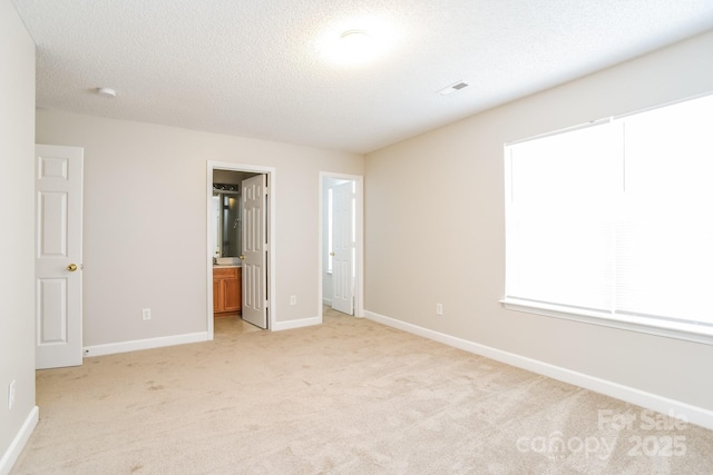 unfurnished bedroom featuring visible vents, baseboards, light colored carpet, ensuite bathroom, and a textured ceiling