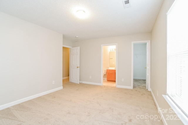 unfurnished bedroom featuring visible vents, light carpet, a closet, baseboards, and a spacious closet