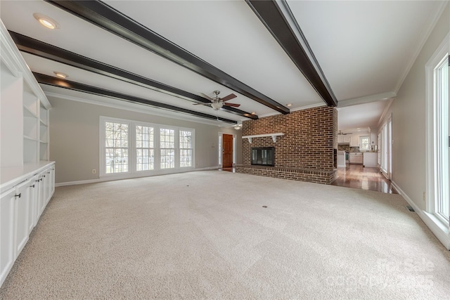 unfurnished living room featuring a brick fireplace, ornamental molding, baseboards, beamed ceiling, and a ceiling fan