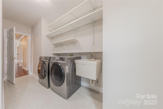 clothes washing area featuring baseboards, a sink, laundry area, and washer and clothes dryer