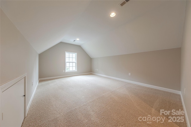 additional living space featuring light carpet, baseboards, visible vents, and vaulted ceiling