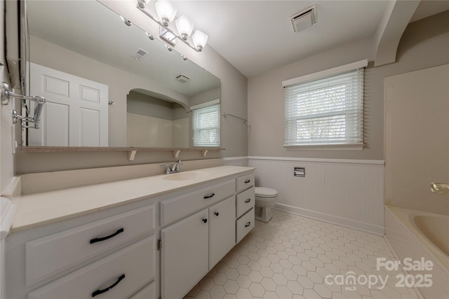 full bathroom featuring a bathing tub, a wainscoted wall, toilet, and visible vents