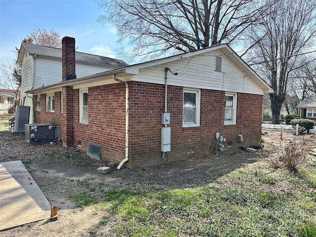 view of side of home featuring brick siding, a chimney, and central AC