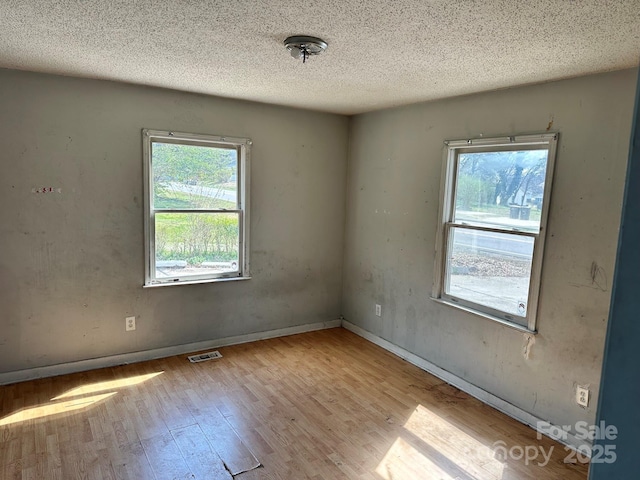 empty room featuring baseboards, wood finished floors, visible vents, and a textured ceiling