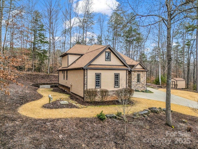 view of side of property featuring stone siding, an outbuilding, concrete driveway, and a shingled roof