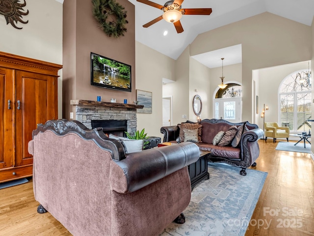 living room featuring light wood-type flooring, high vaulted ceiling, a stone fireplace, and ceiling fan