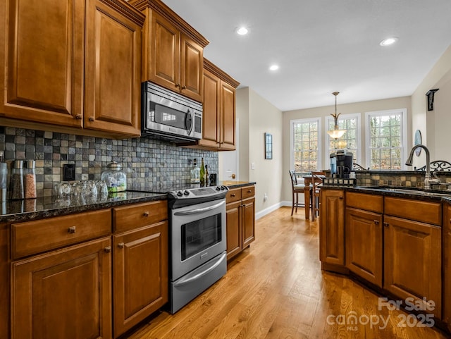 kitchen featuring light wood-type flooring, a sink, backsplash, appliances with stainless steel finishes, and brown cabinetry