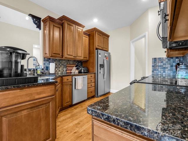 kitchen with light wood-type flooring, a sink, stainless steel appliances, tasteful backsplash, and brown cabinets