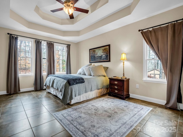 bedroom with multiple windows, a raised ceiling, and baseboards