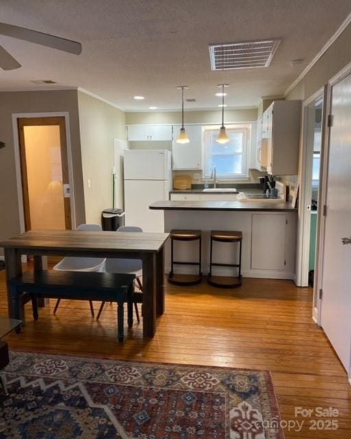 kitchen featuring visible vents, a peninsula, freestanding refrigerator, a sink, and light wood-style floors