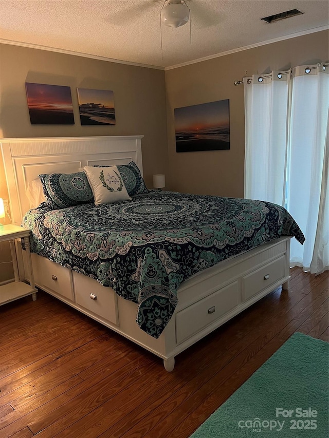 bedroom with visible vents, a textured ceiling, crown molding, and wood finished floors