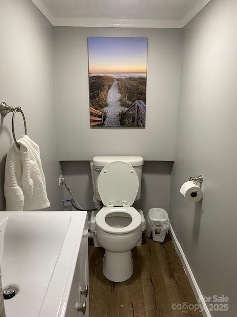 bathroom with baseboards, toilet, ornamental molding, wood finished floors, and a sink