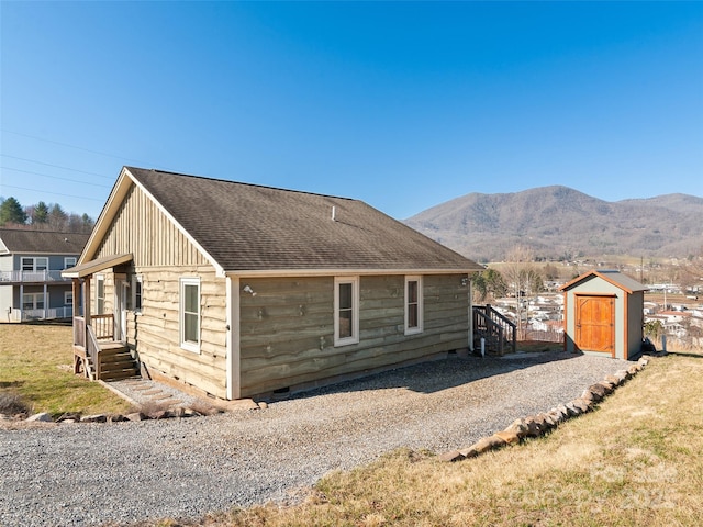 view of front facade with a shingled roof, an outdoor structure, a storage unit, crawl space, and a mountain view