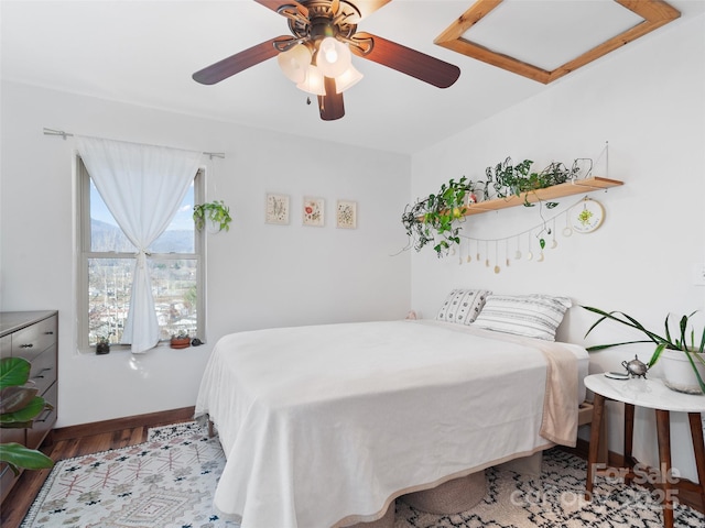 bedroom featuring baseboards, attic access, wood finished floors, and a ceiling fan