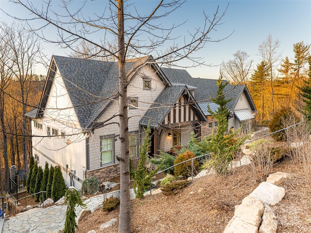 view of front facade featuring fence, stone siding, and roof with shingles