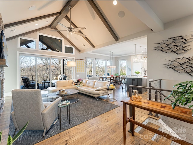 living room featuring high vaulted ceiling, light wood-style flooring, a fireplace, ceiling fan, and beamed ceiling