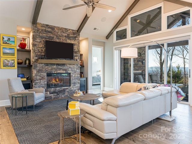 living room with visible vents, beam ceiling, wood finished floors, a stone fireplace, and ceiling fan