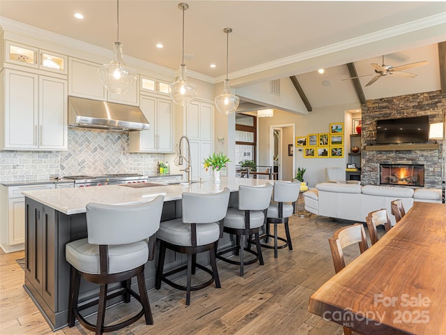 kitchen with light countertops, an island with sink, light wood-style floors, and under cabinet range hood