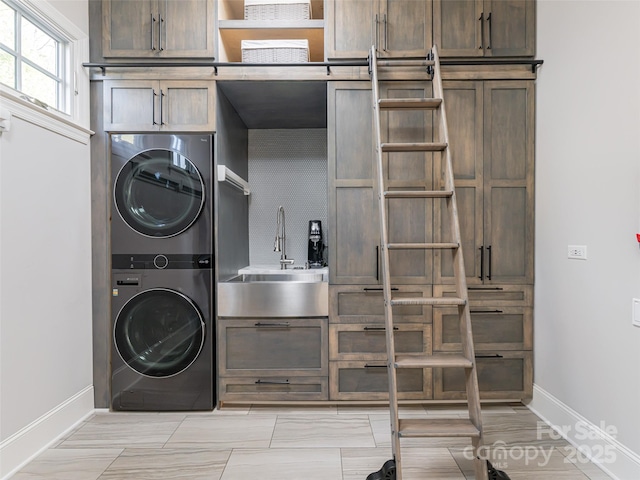 laundry area featuring baseboards, cabinet space, stacked washer and clothes dryer, and a sink