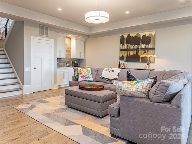 living room featuring visible vents, baseboards, stairway, light wood-type flooring, and recessed lighting