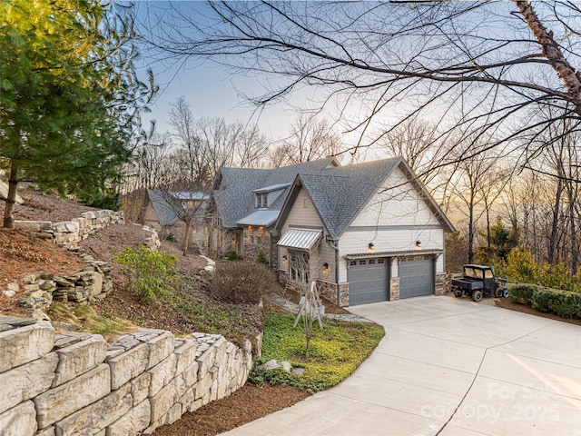 view of front facade featuring an attached garage, stone siding, driveway, and roof with shingles