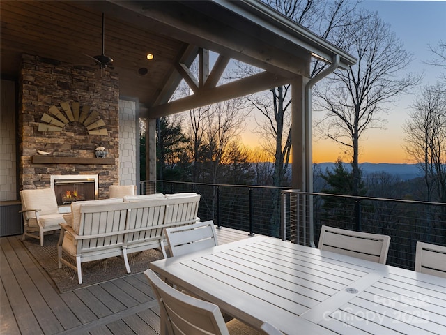 deck at dusk featuring an outdoor living space with a fireplace, outdoor dining space, and a ceiling fan