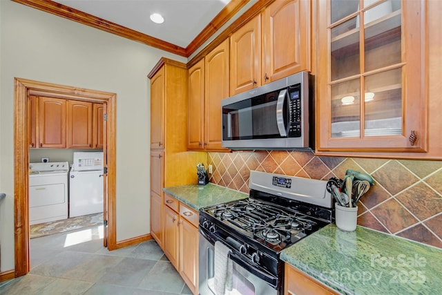 kitchen featuring washing machine and clothes dryer, glass insert cabinets, ornamental molding, decorative backsplash, and appliances with stainless steel finishes