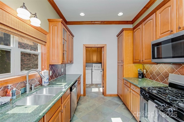 kitchen with stone countertops, a sink, ornamental molding, appliances with stainless steel finishes, and washer and clothes dryer