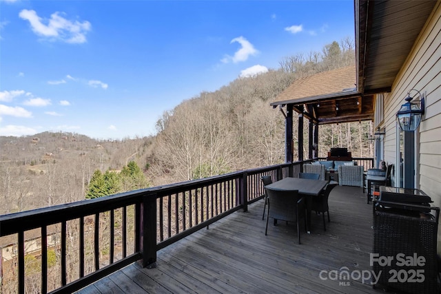 wooden deck featuring outdoor dining space and a wooded view