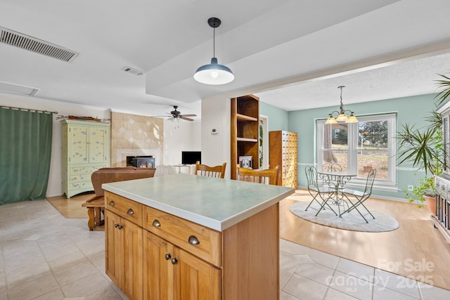 kitchen featuring visible vents, a kitchen island, a tiled fireplace, decorative light fixtures, and ceiling fan with notable chandelier