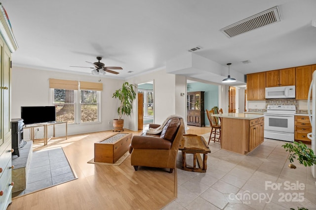 living area with visible vents, ornamental molding, and a ceiling fan