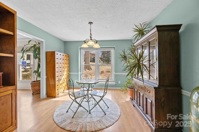 dining area with baseboards, light wood-type flooring, and a textured ceiling