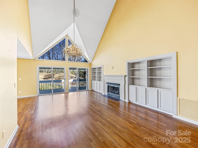 unfurnished living room with visible vents, a fireplace with flush hearth, built in shelves, wood finished floors, and a chandelier