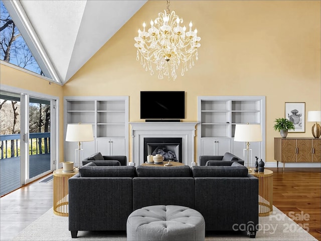 living area featuring a glass covered fireplace, a notable chandelier, wood finished floors, and high vaulted ceiling