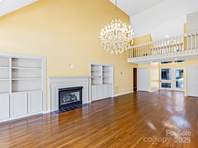 unfurnished living room featuring built in shelves, a notable chandelier, a fireplace with flush hearth, high vaulted ceiling, and wood finished floors